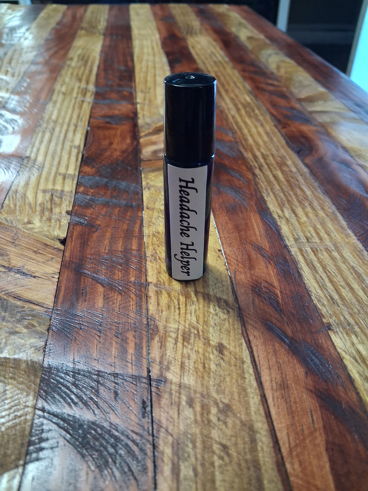 Dark roll-on bottle with a black cap and white label standing upright on a wood-grain surface.